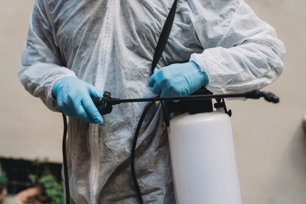 Sanitation worker in protective suit holding a sprayer. 